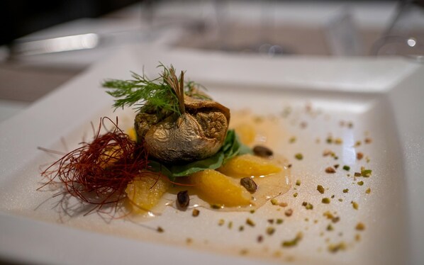 A plated dish with a central nut, garnished with herbs and a red garnish, surrounded by yellow elements and sprinkled with green herbs.