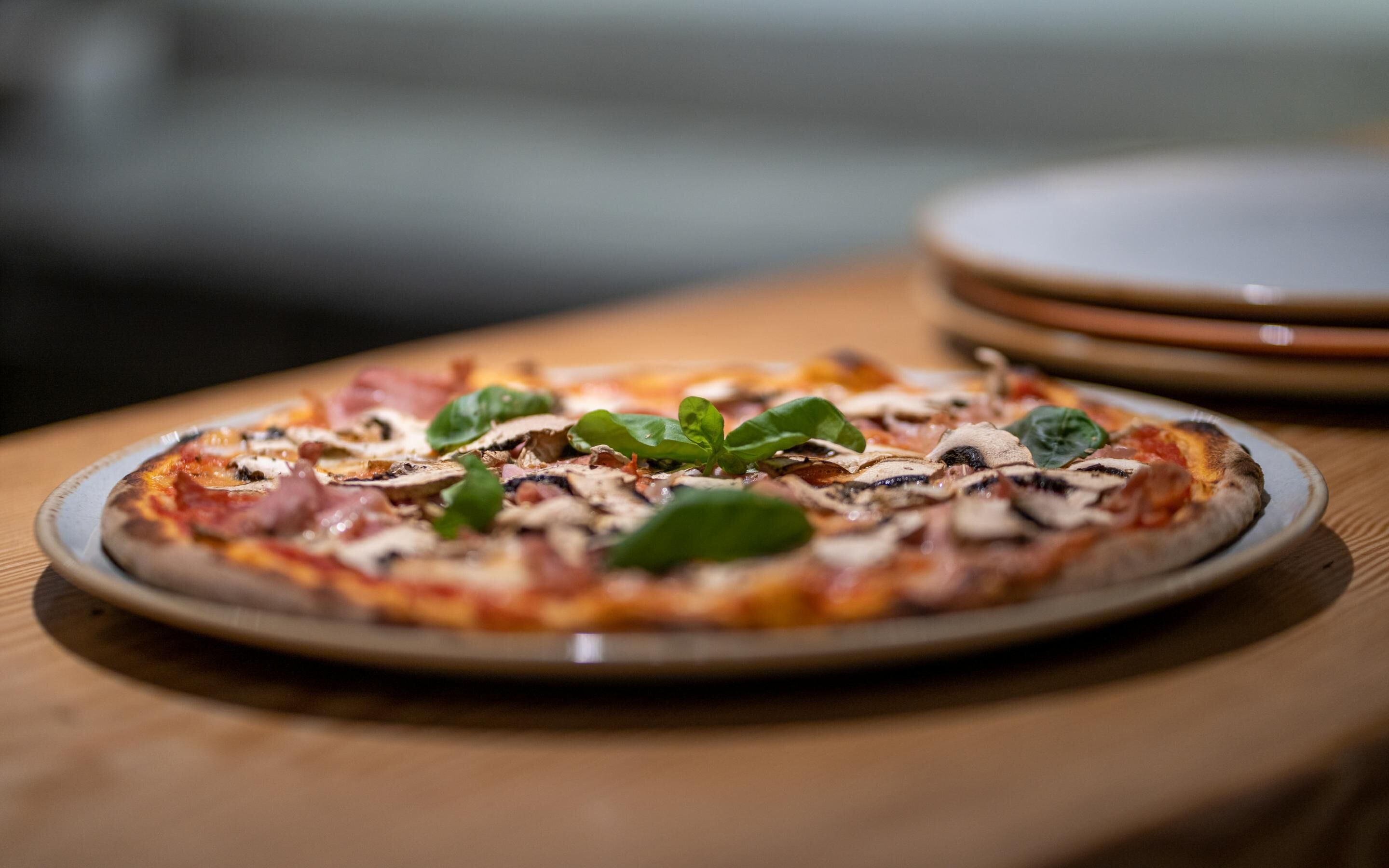 Una pizza su un piatto con condimenti e foglie di basilico.