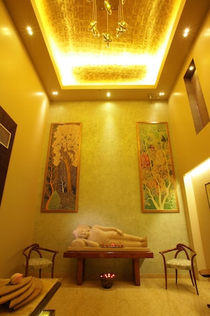A spa room with a massage table, two chairs, and wall-mounted artwork. - Justa Gurgaon (Gurugram)