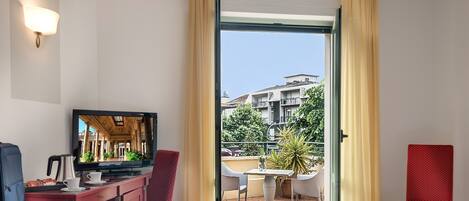 A hotel room with a television, a desk with a coffee maker, and a view of a balcony with outdoor furniture.
