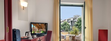 Habitación de hotel con televisión, escritorio con cafetera y vista a un balcón con mobiliario exterior.
