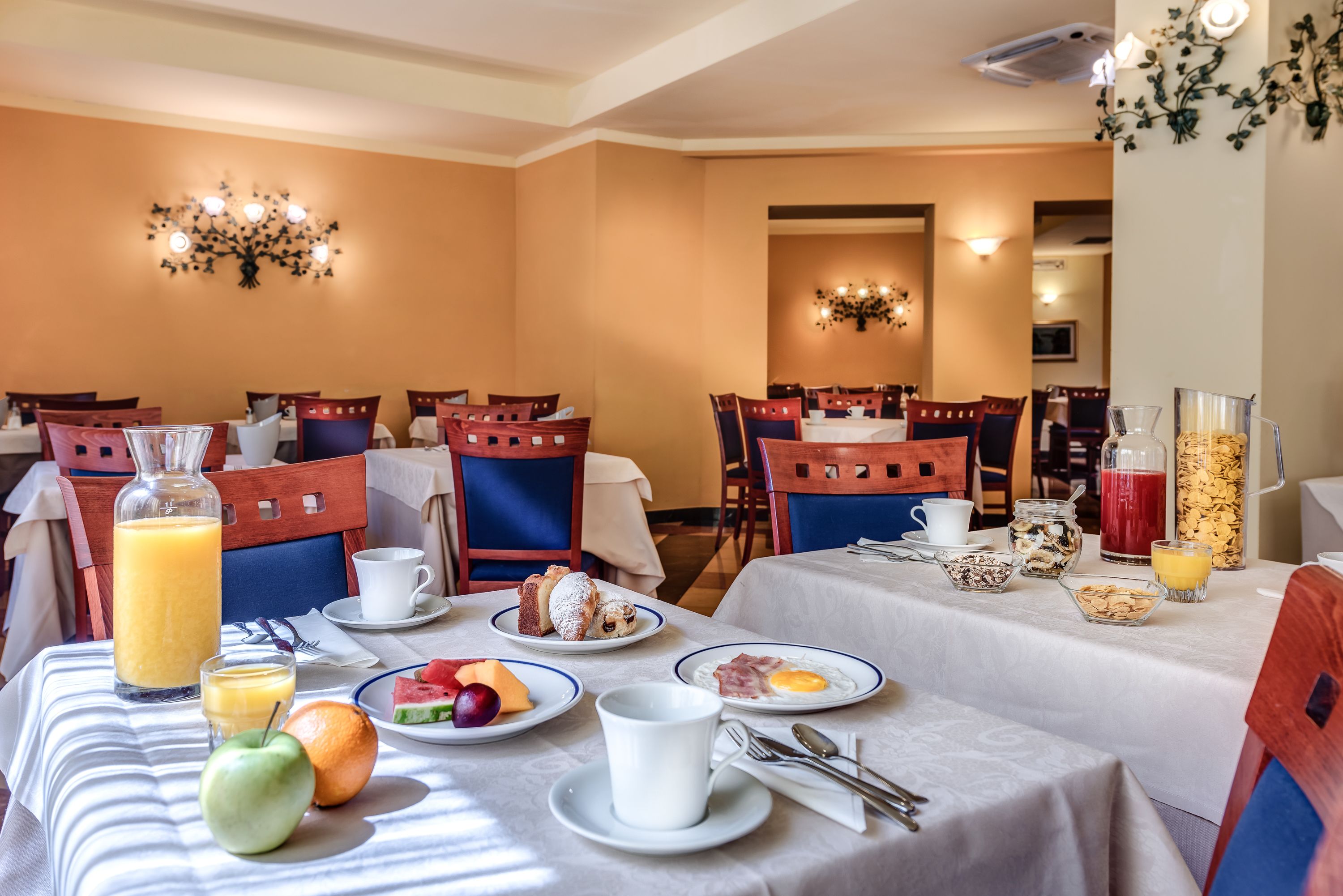 Comedor con mesas dispuestas para el desayuno, incluyendo platos de comida, bebidas y productos para el desayuno.