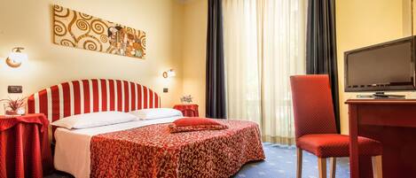 A hotel room with a bed, a desk with a television, and a chair.