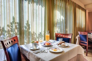 Una mesa de desayuno servida con platos de comida, una jarra de zumo de naranja y un vaso de zumo de naranja.