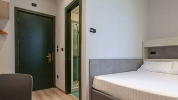 Una camera d'albergo con un letto, una scrivania, una sedia, una porta e un appendiabiti.