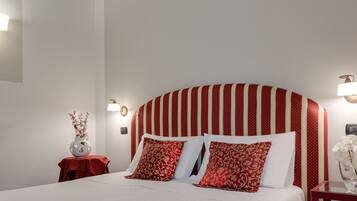Une chambre d’hôtel avec un grand lit, une tête de lit à rayures rouges, deux tables de chevet avec des lampes et un vase rempli de fleurs posé sur l’une des tables.