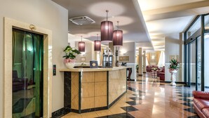 Un vestíbulo de hotel con un mostrador de recepción, un ascensor de cristal y una mesa de registro.