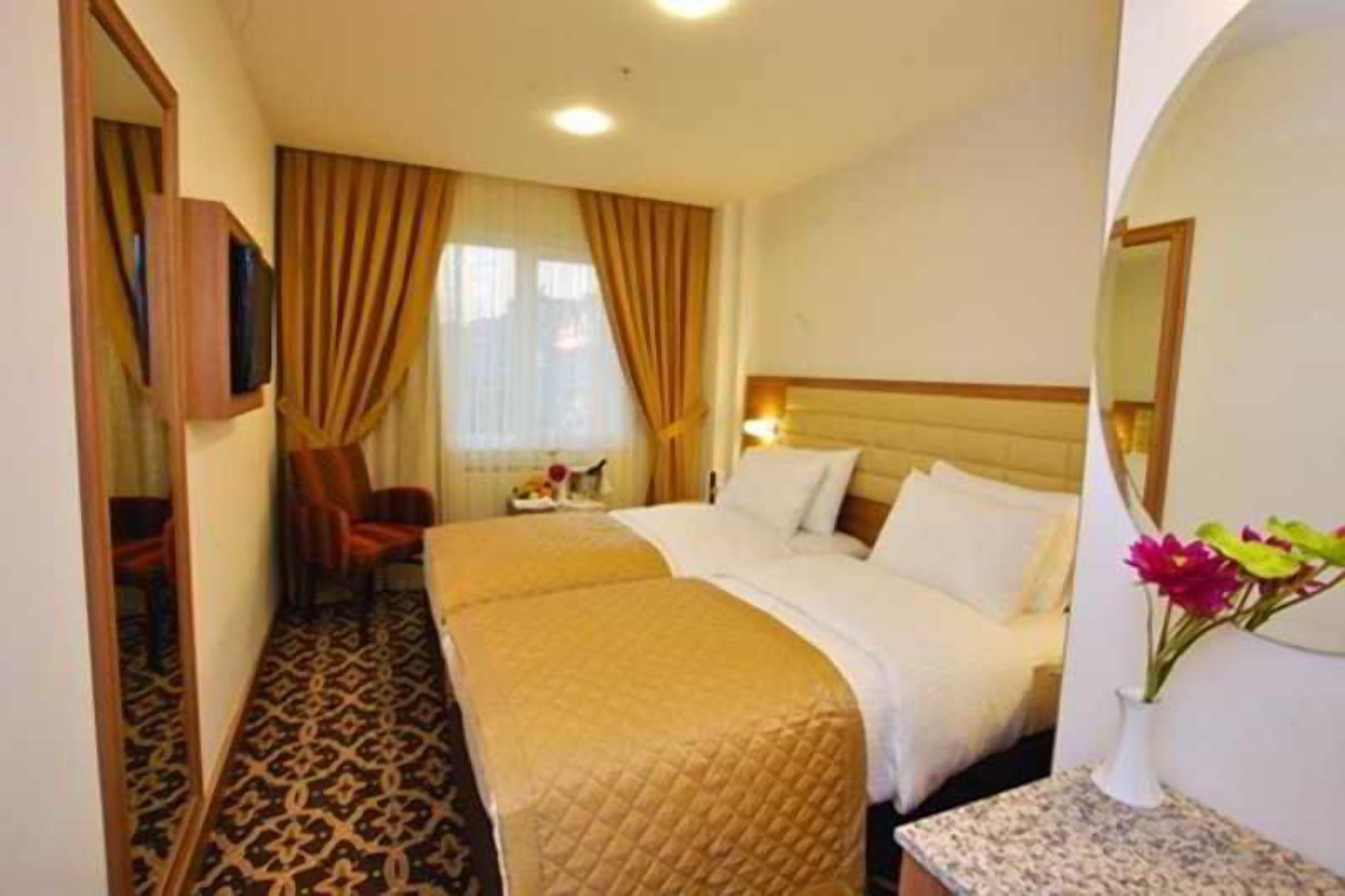 A hotel room with a double bed, a chair, a television, and a small table with a vase of flowers.