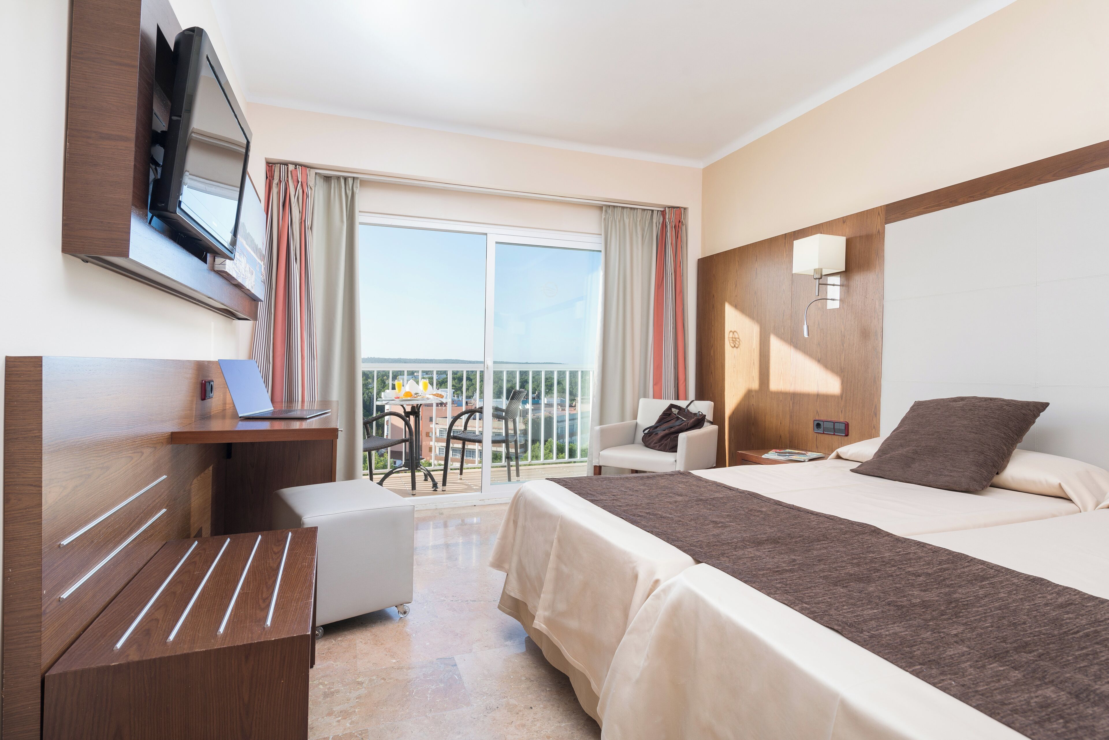 Habitación de hotel con cama, escritorio, silla, televisión y balcón con vistas.