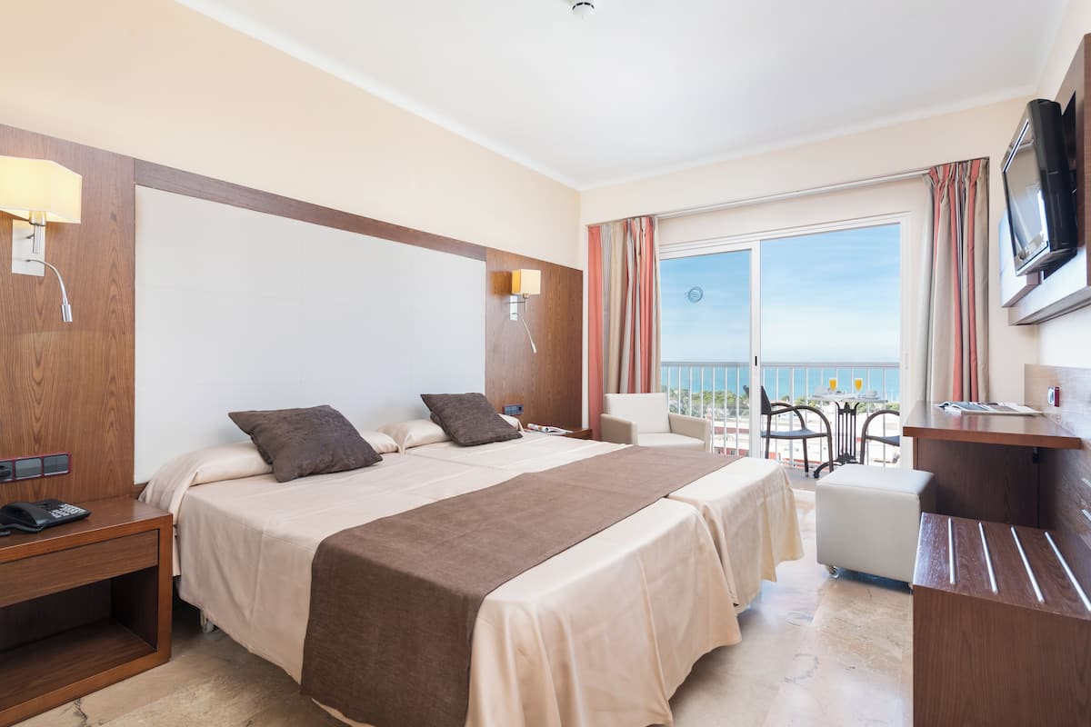 A hotel room with a large bed, a desk, a chair, and a balcony with a view.