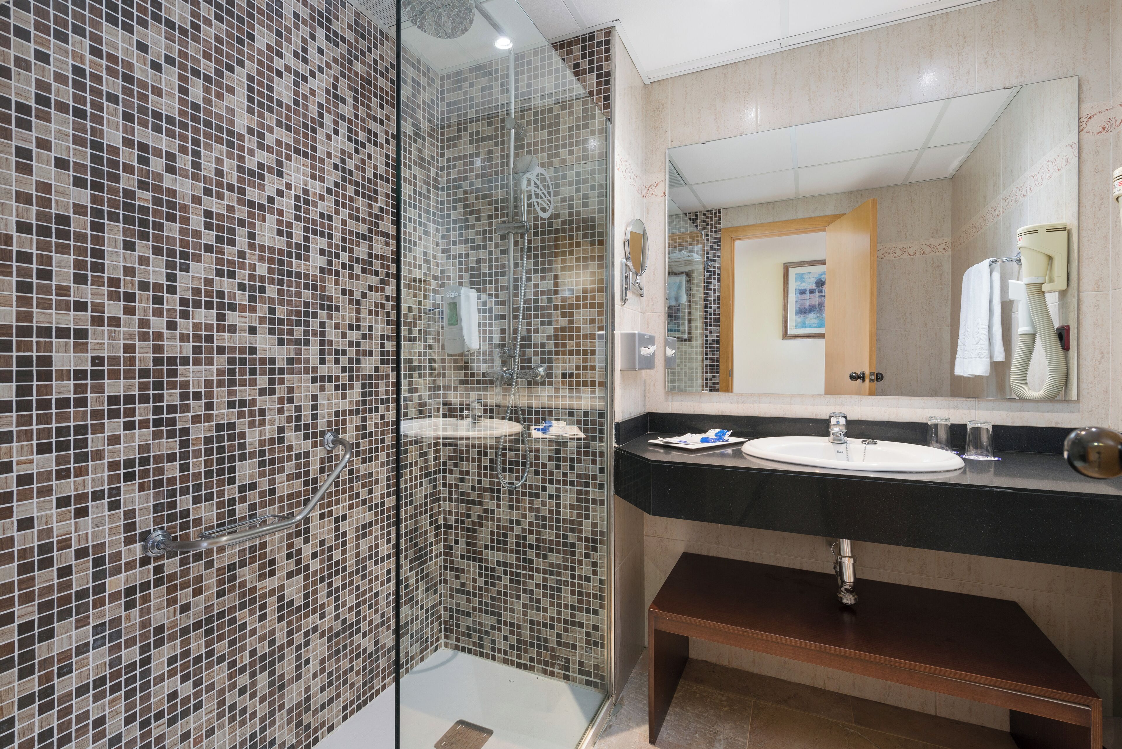 A modern bathroom with mosaic tile walls, a glass-enclosed shower, a sink with a vanity, and a large mirror.