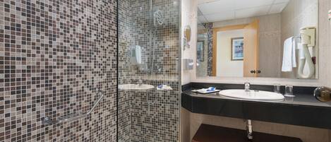 A modern bathroom with mosaic tile walls, a glass-enclosed shower, a sink with a vanity, and a large mirror.