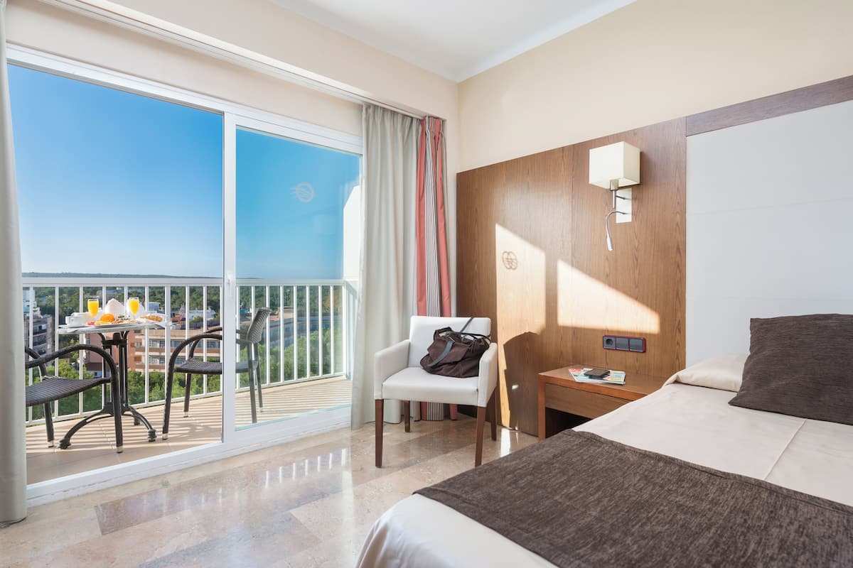 A hotel room with a balcony, a bed, a desk, and a chair.