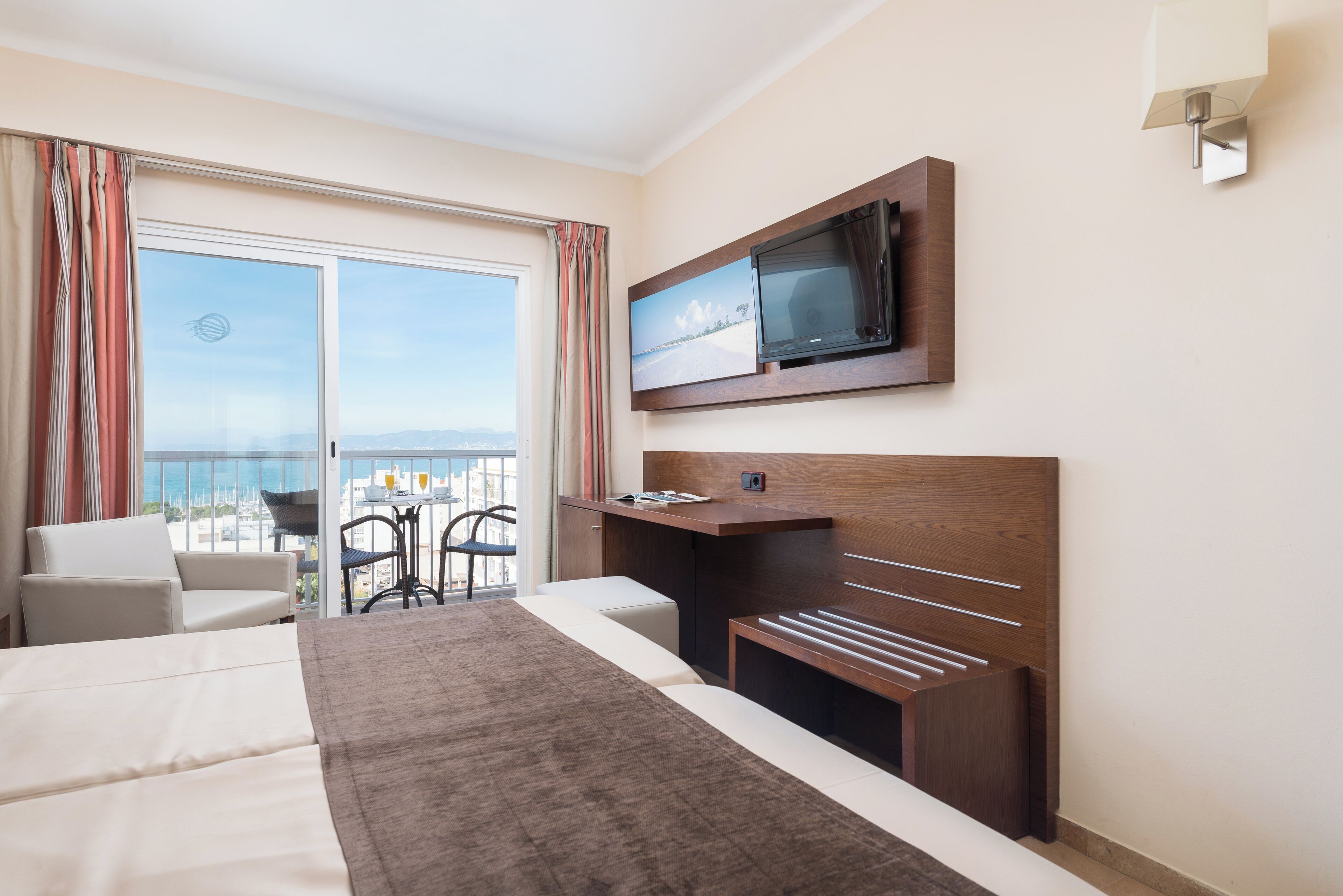 Habitación de hotel con una cama grande, televisión montada en la pared, balcón con vistas y un escritorio.