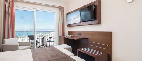 Habitación de hotel con una cama grande, televisión montada en la pared, balcón con vistas y un escritorio.