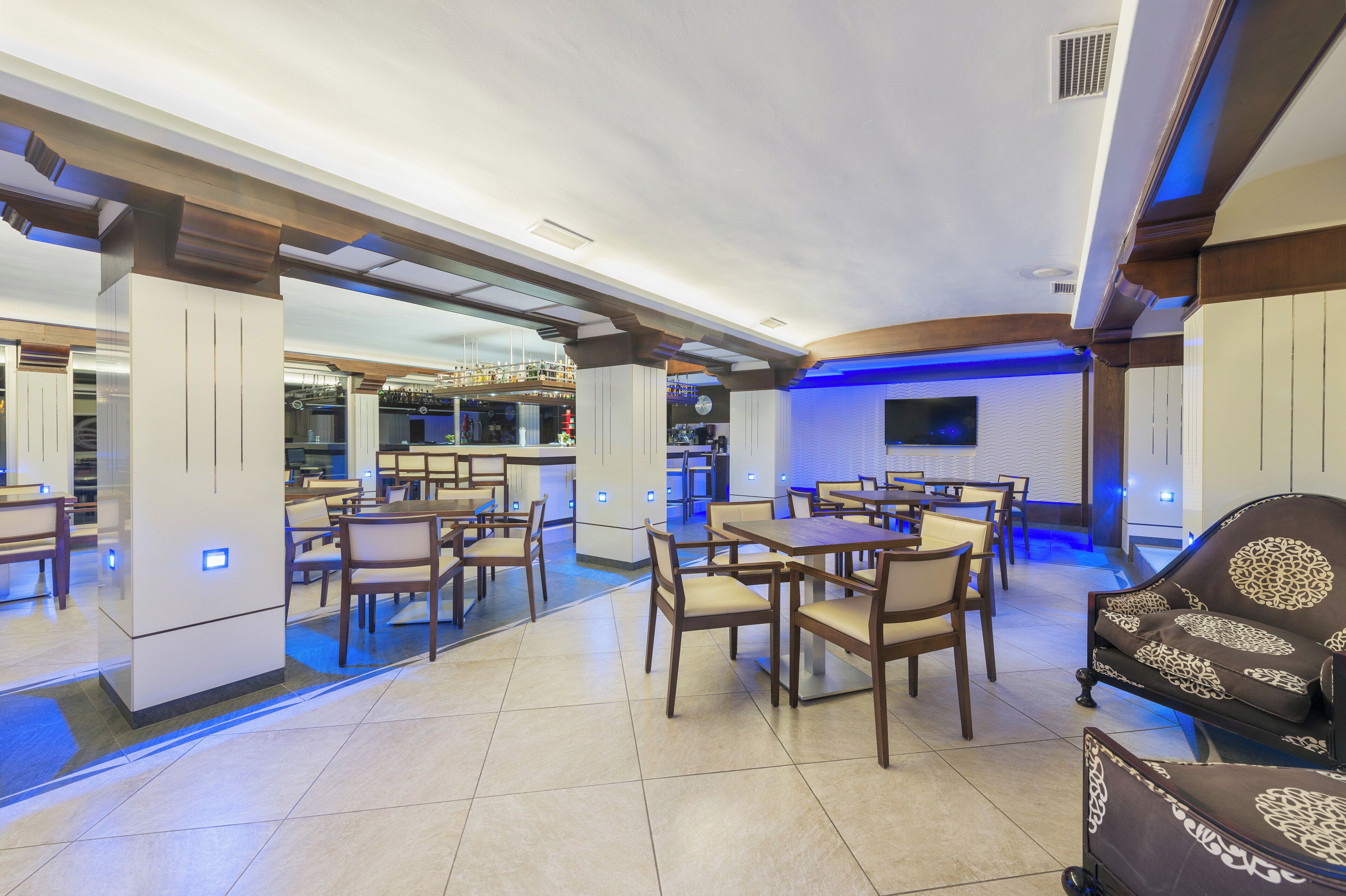 A spacious restaurant with high ceilings, modern lighting, and a variety of seating arrangements including tables and chairs.
