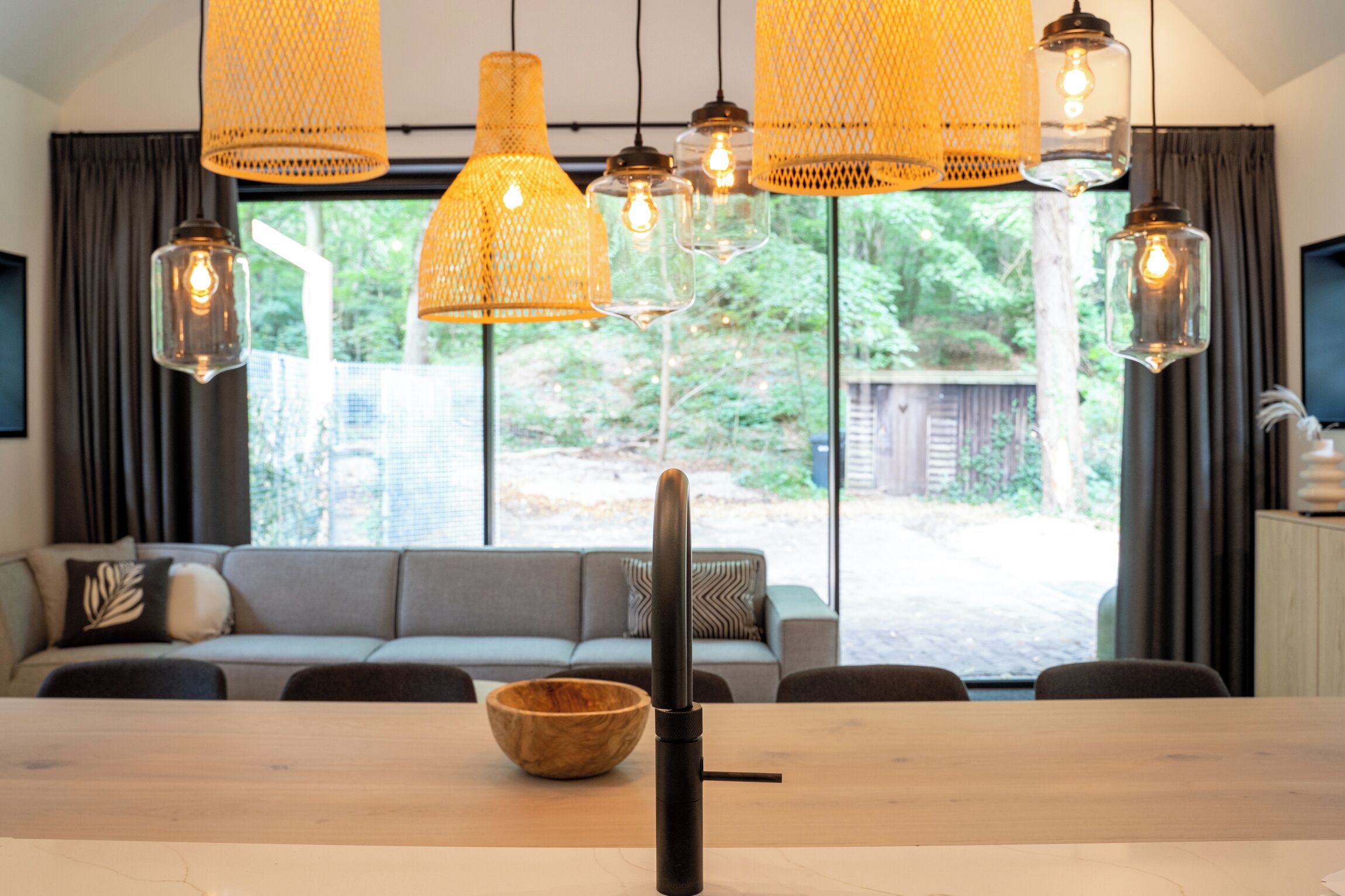 Een eetgedeelte met een houten tafel, een geweven mand en hangende rieten lampen.