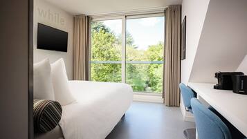 A hotel room with a bed, a desk, a chair, a TV, and a window with curtains.