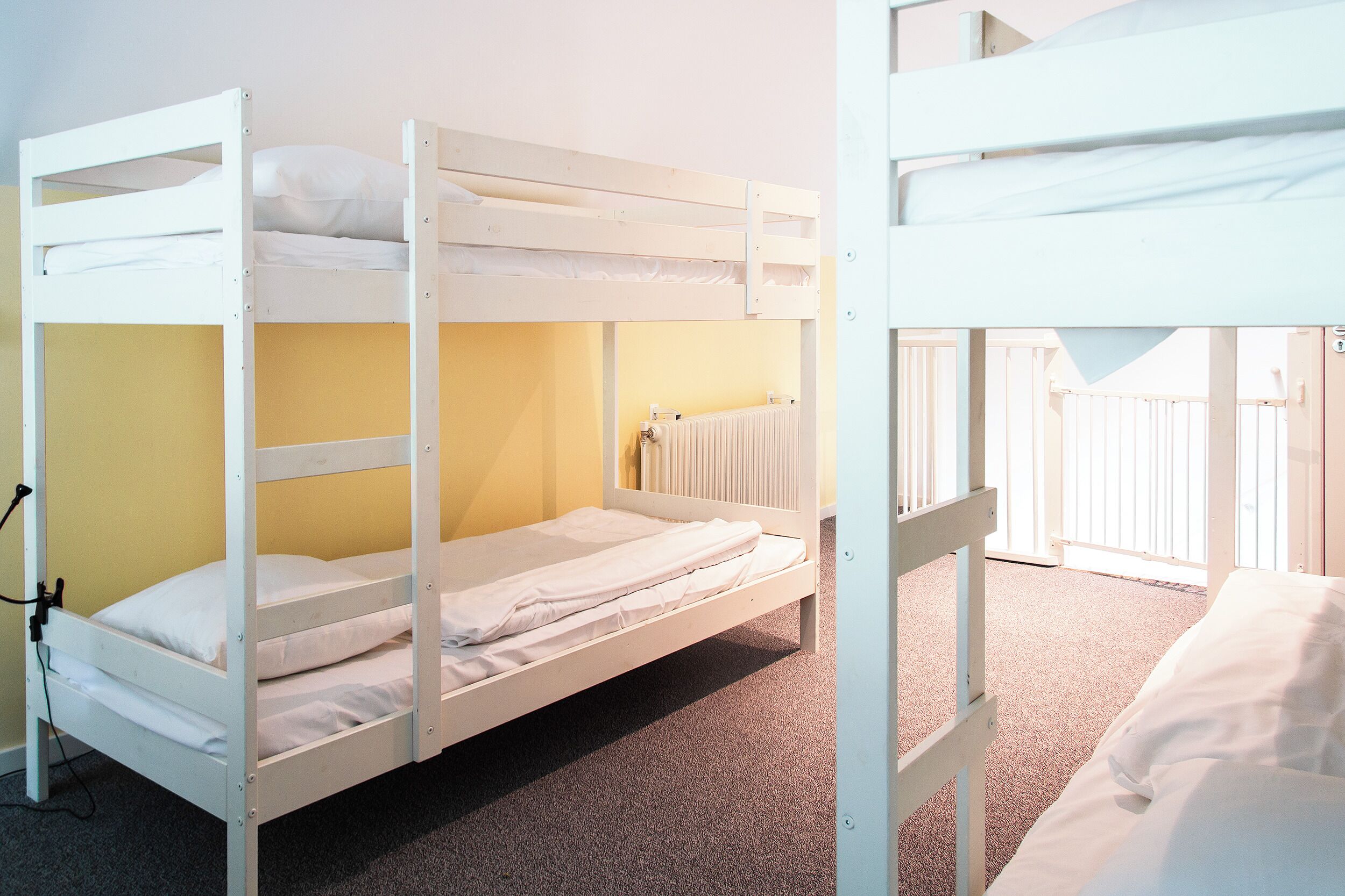 Dormitorio con literas, radiador, suelo alfombrado y ventana con persianas.