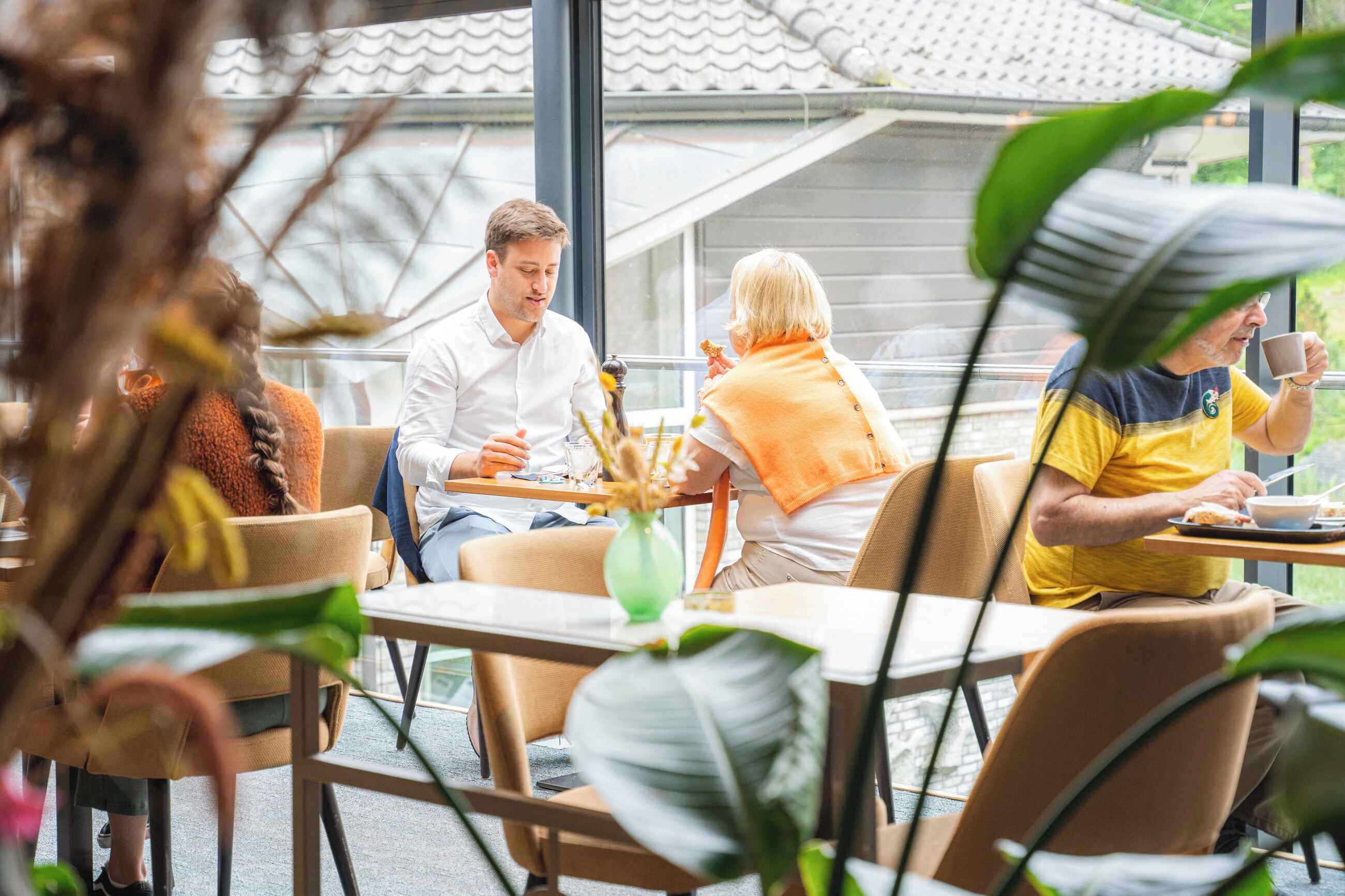 A café with tables and chairs, large windows, and indoor plants.