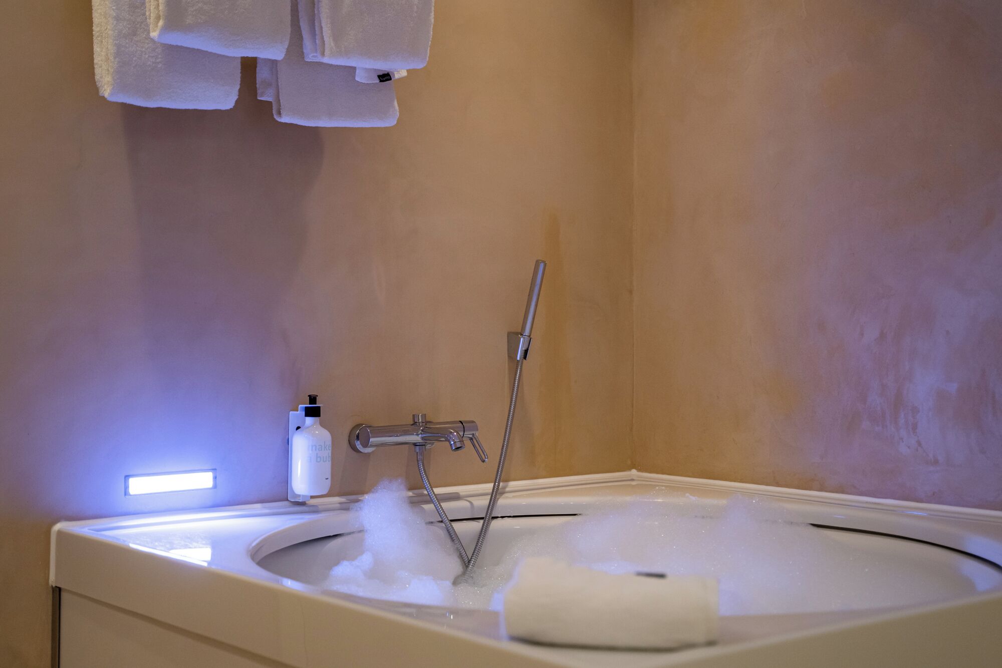 Un baño con bañera, cabezal de ducha manual y una botella de jabón.