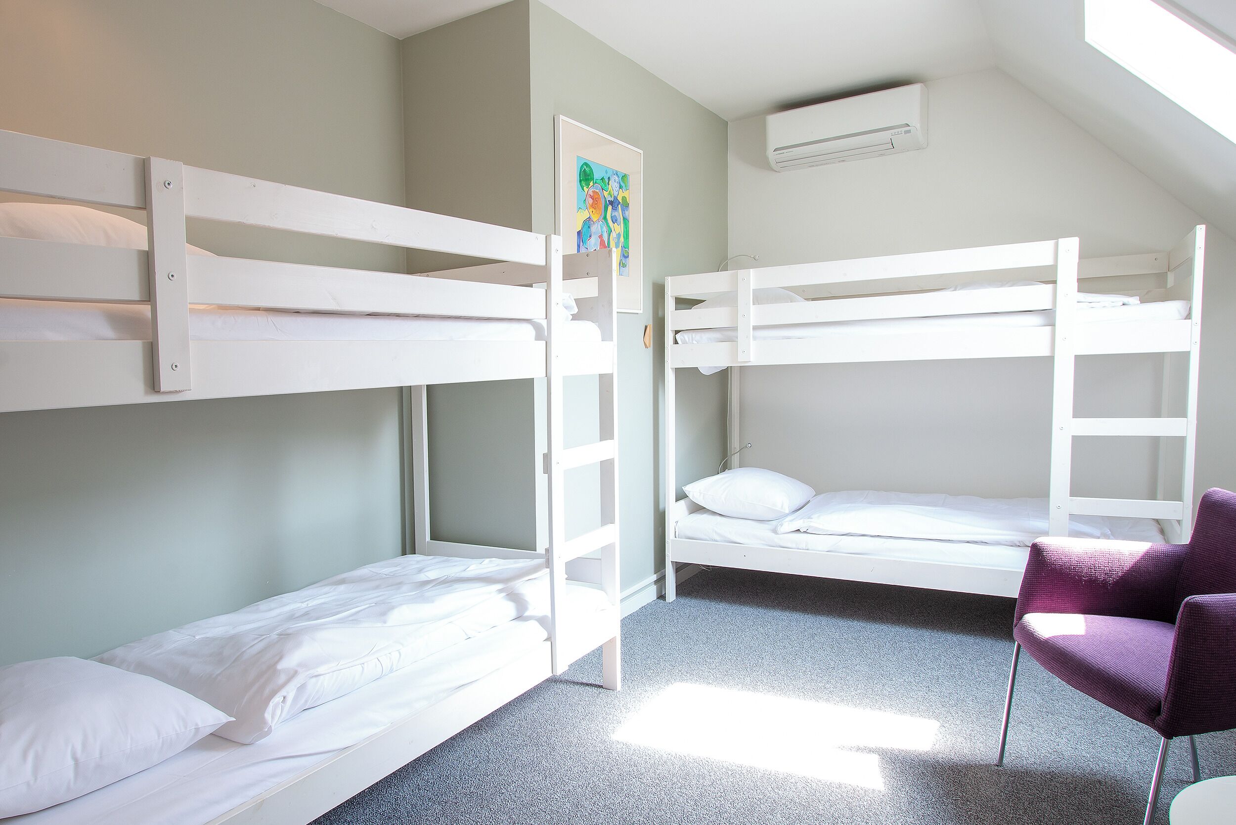 Una habitación con dos literas, una silla morada y un cuadro en la pared.