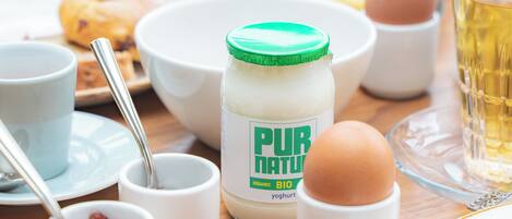 Un desayuno con un tarro de yogur orgánico, huevos, una taza de té y un muffin sobre una mesa de madera.