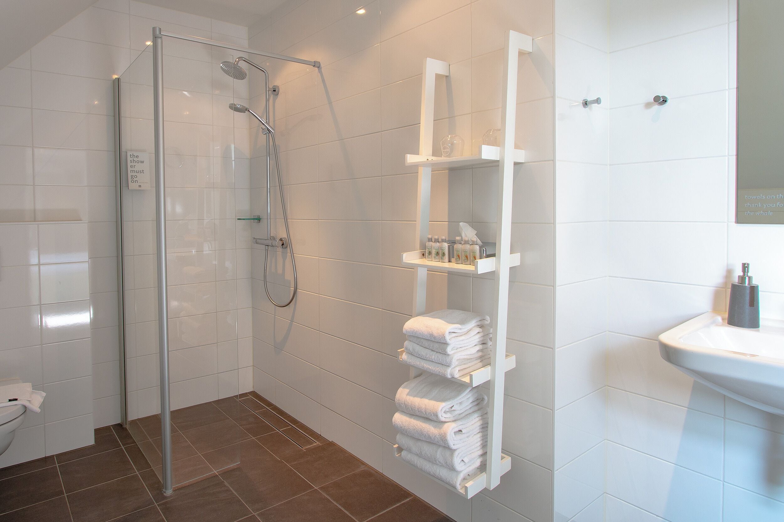 A modern bathroom with a glass-enclosed shower, a white sink, and a towel rack with neatly folded towels.