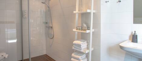 A modern bathroom with a glass-enclosed shower, a white sink, and a towel rack with neatly folded towels.