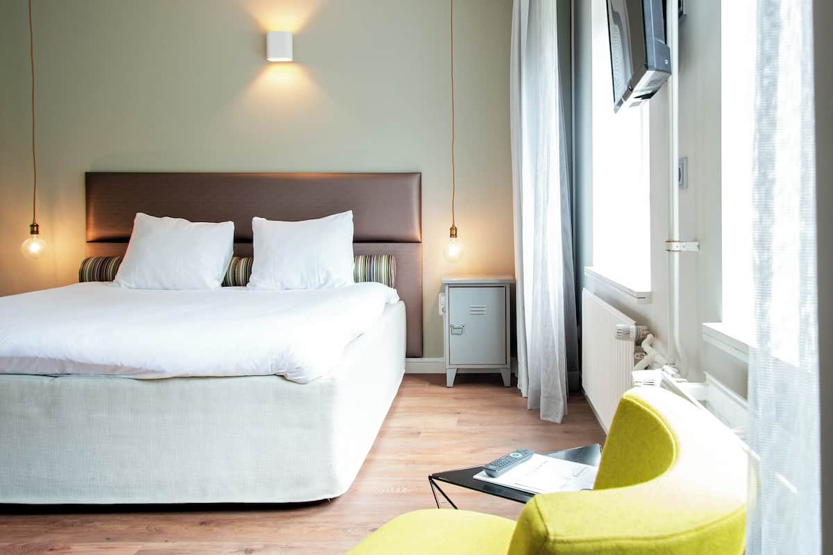 A hotel room with a large bed, bedside table, and a chair.