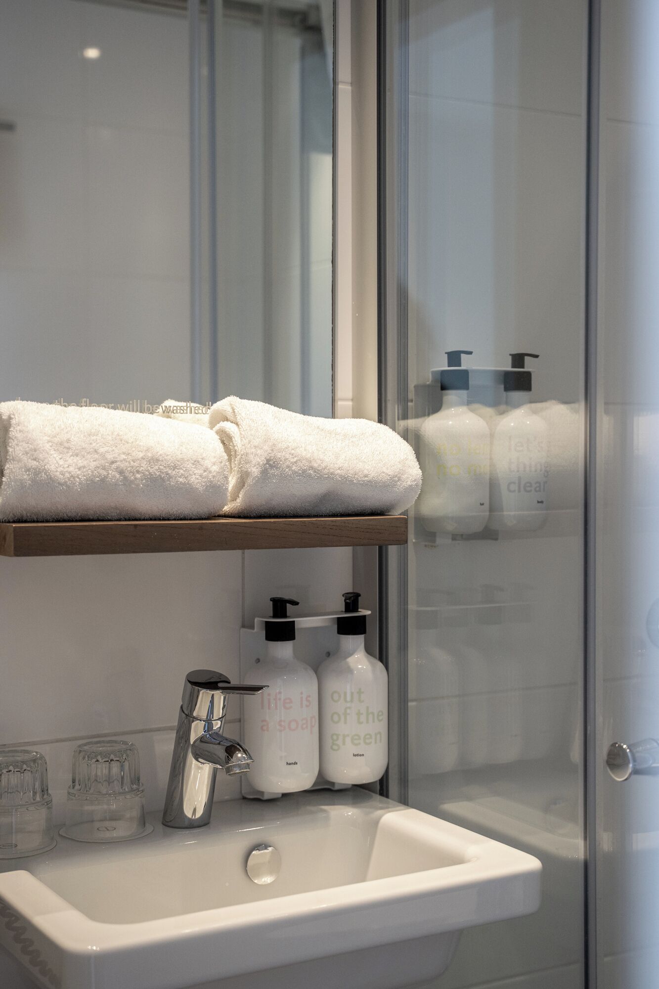 Une salle de bain avec une douche à parois de verre, un lavabo blanc avec un miroir et une étagère sur laquelle est posée une serviette pliée.