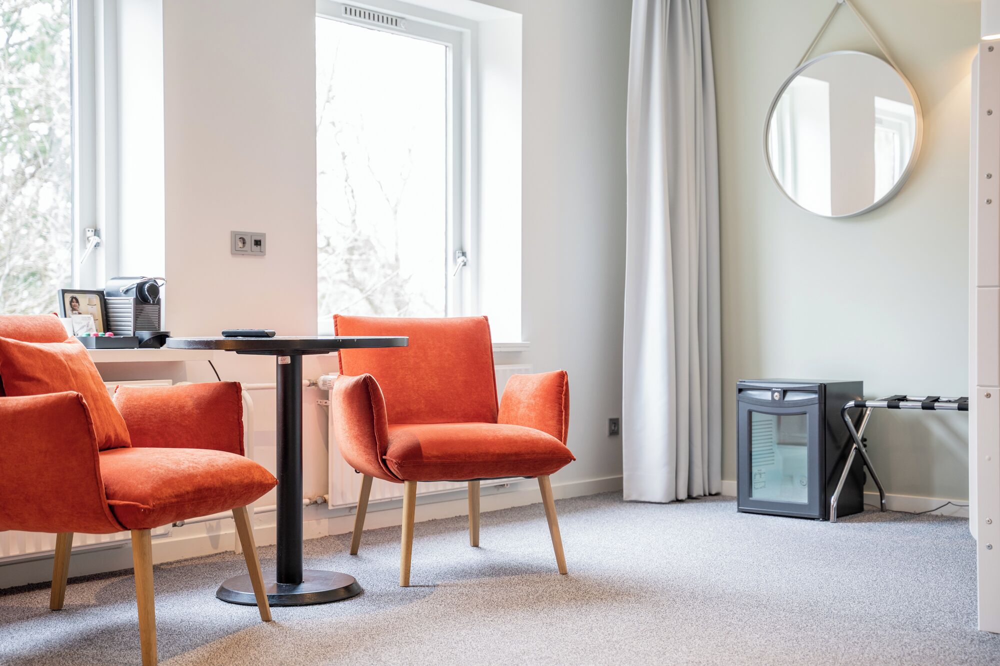 A modern room with two orange chairs, a small round table, a mirror, and a compact heater.