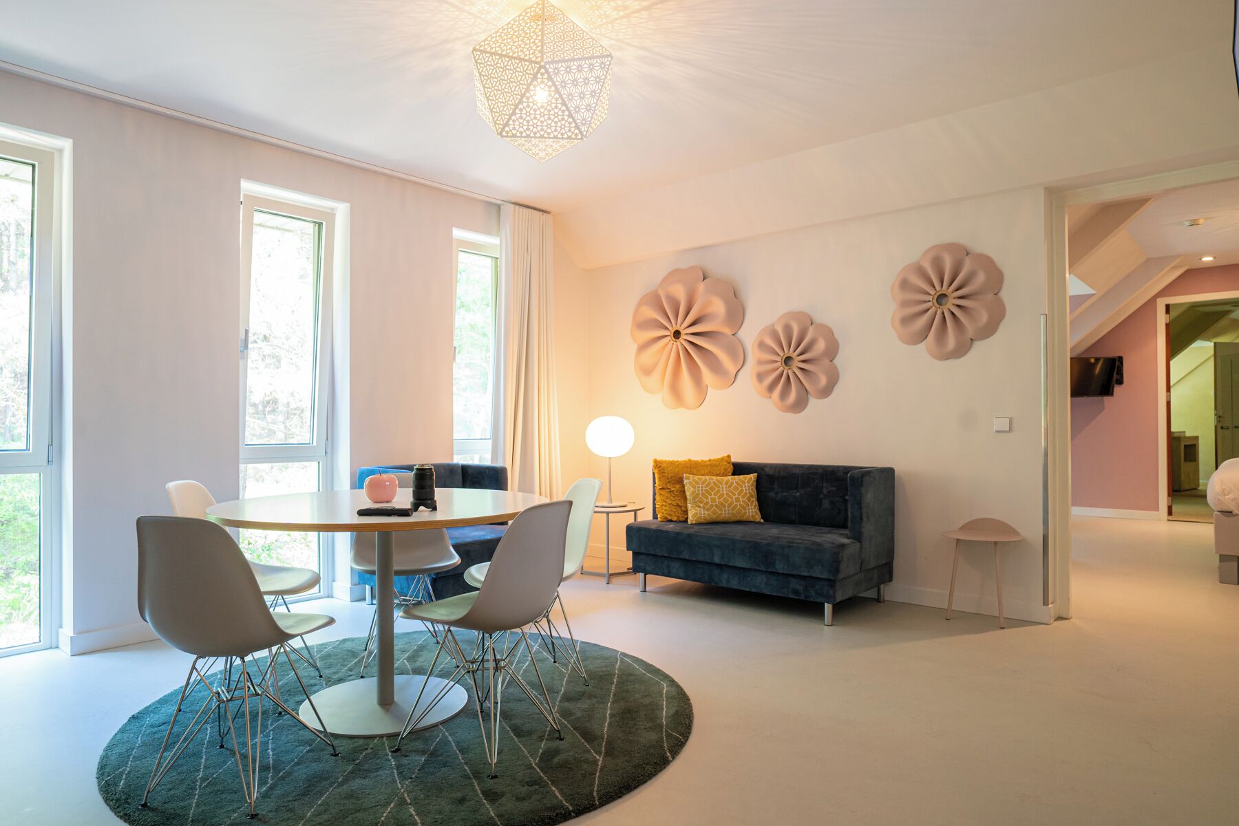 A modern living room with a round dining table, two chairs, a sofa, and decorative wall art.