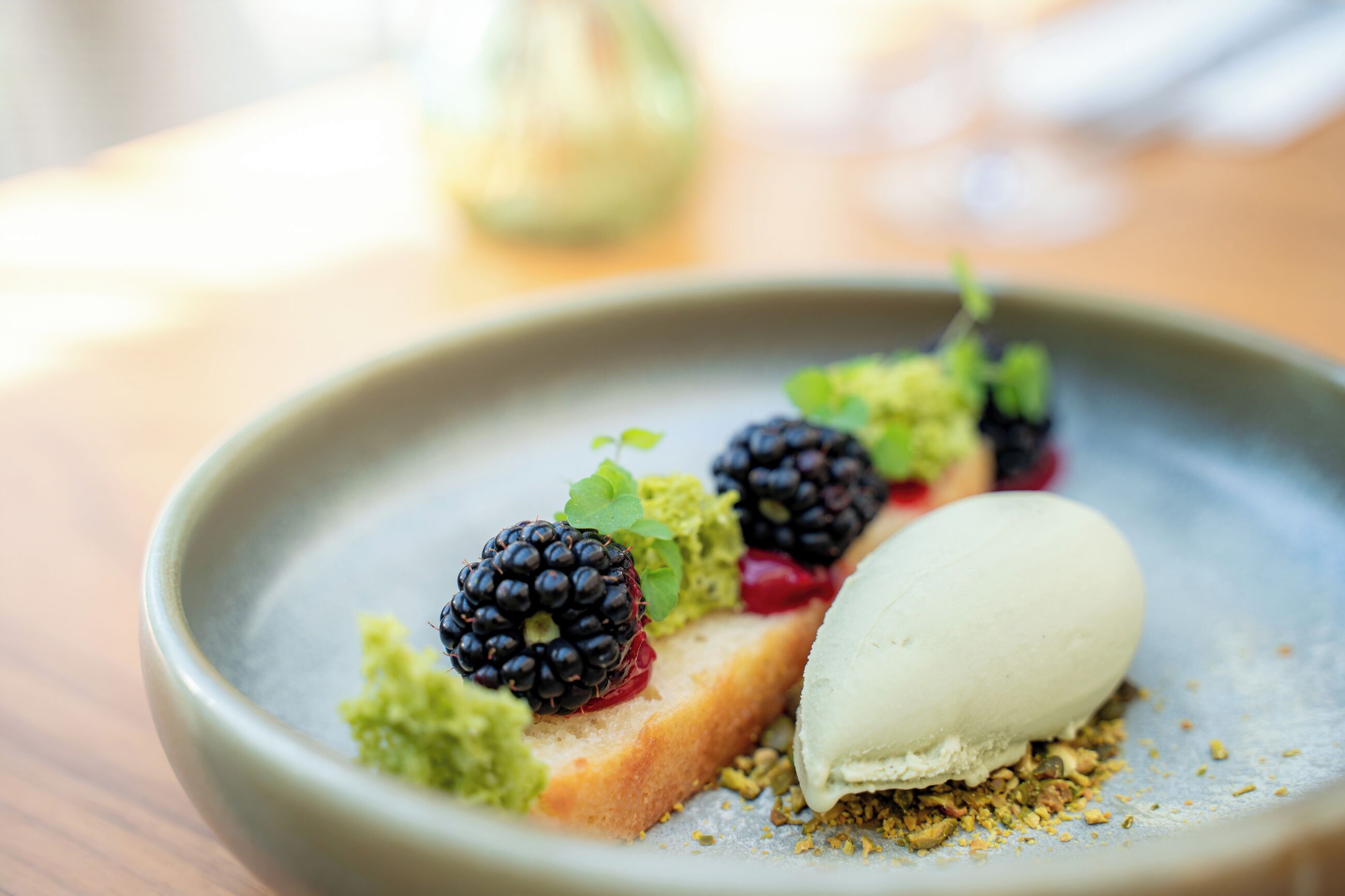 Un plato de postre con una bola de helado, moras y un trozo de pastel.