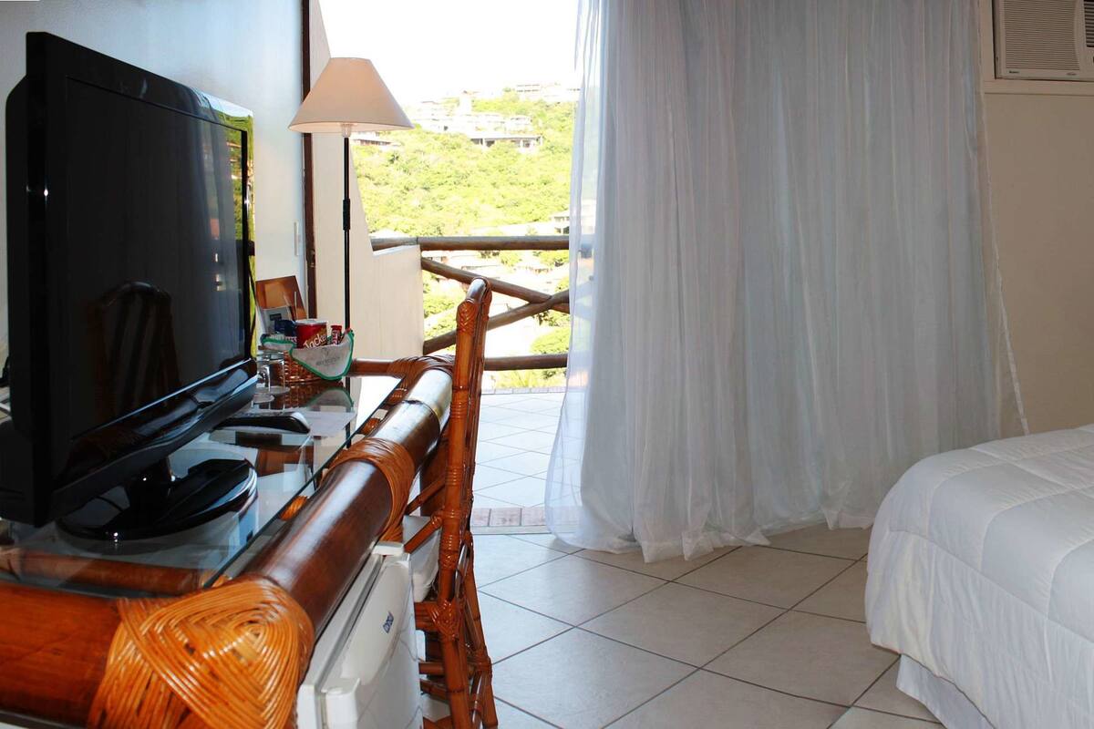 Habitación de hotel con una cama grande, televisión, escritorio con computadora y balcón con mesa y sillas.