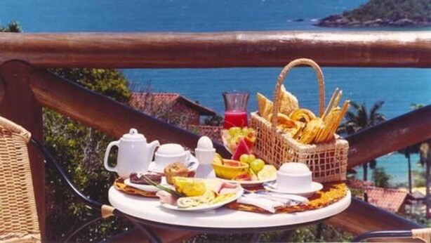 Un plateau de petit-déjeuner avec une variété d’aliments et une boisson, placé de manière à offrir une vue panoramique sur la côte.