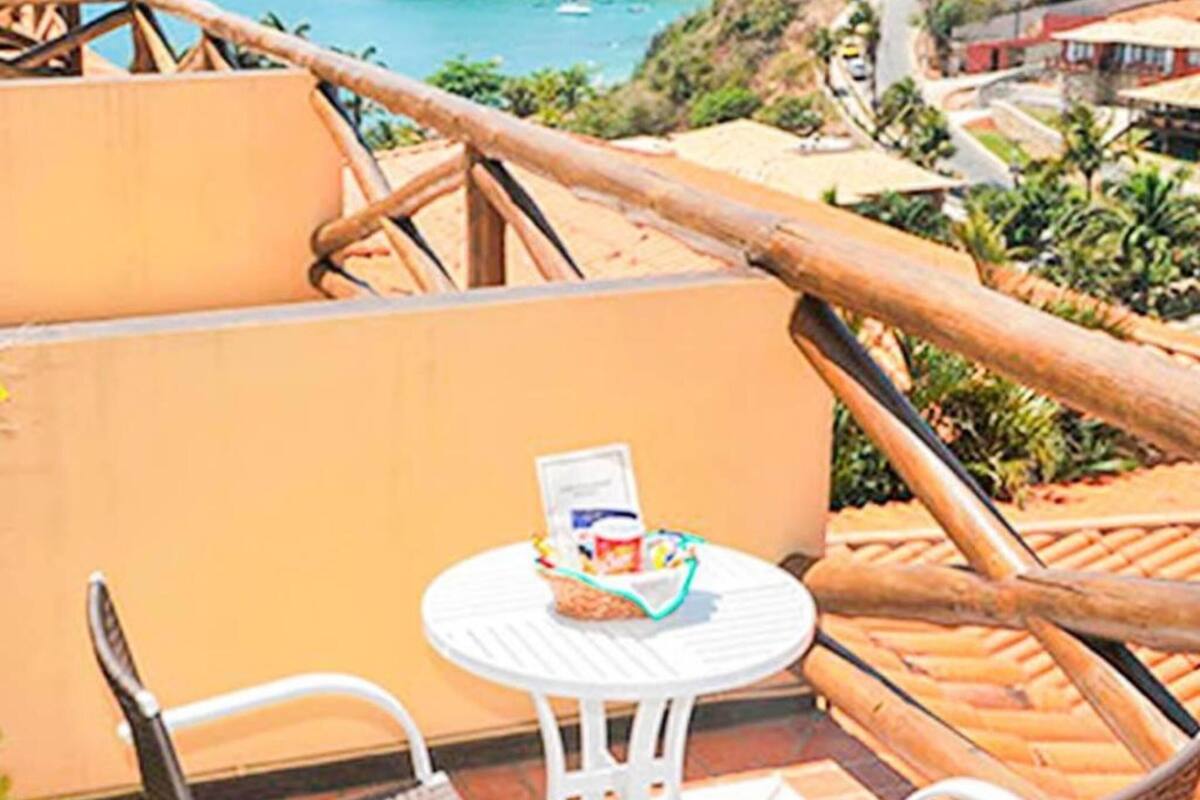 Un balcón con mobiliario de mimbre, una pequeña mesa con una cesta y una vista panorámica de la costa.