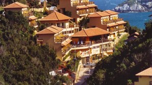Un hôtel situé sur la côte, doté de nombreux balcons, de toits en tuiles de terre cuite et offrant une vue sur la mer.