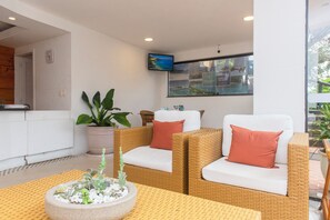 Un espacio de sala moderno con muebles de mimbre, un televisor de pantalla plana montado en la pared y una planta en maceta.