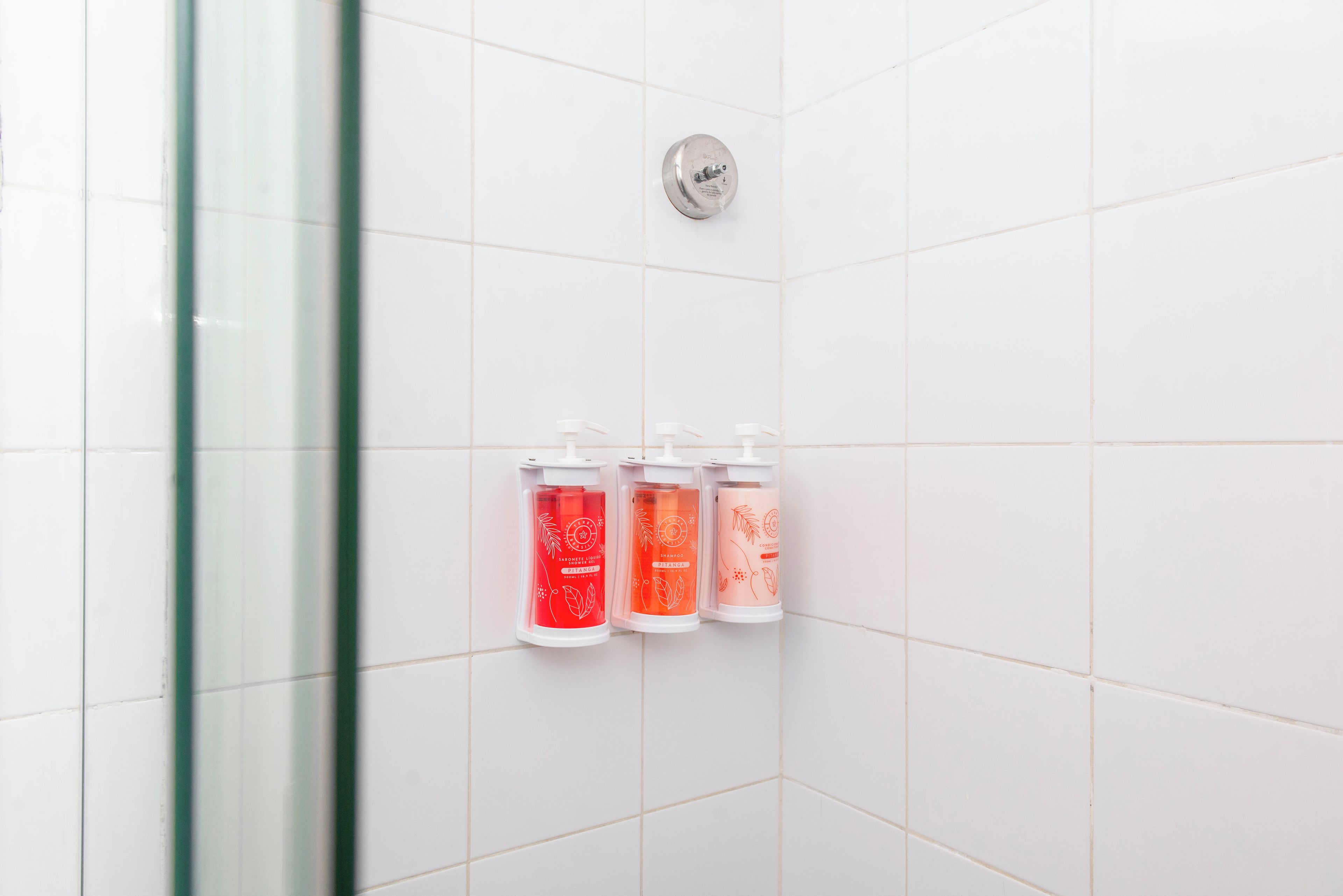 A bathroom with white tiles, a glass shower enclosure, and three dispensers for liquid soap.