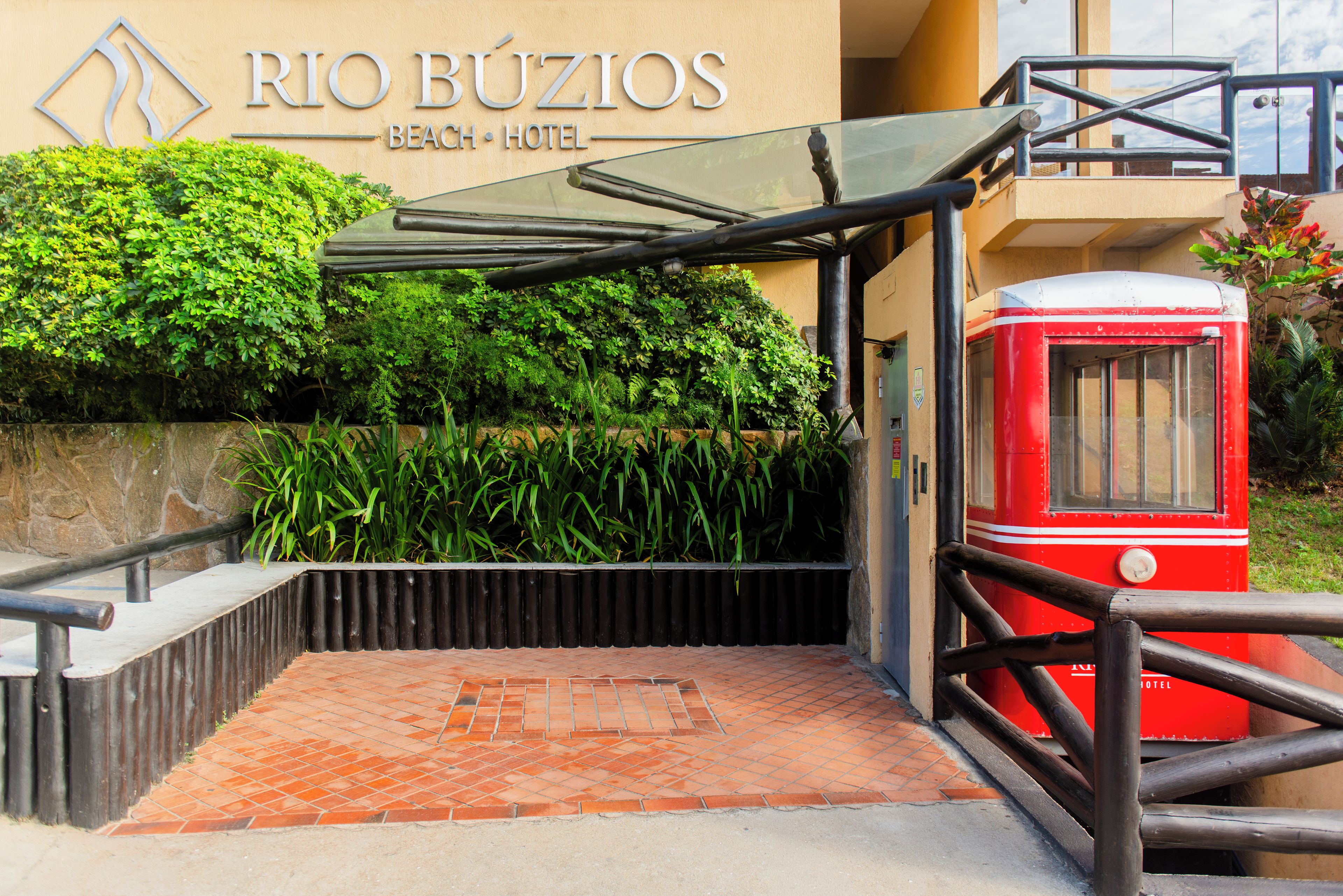 The entrance to Rio Búzios Beach Hotel with a covered walkway, a red tram, and lush greenery.