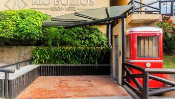 The entrance to Rio Búzios Beach Hotel with a covered walkway, a red tram, and lush greenery.