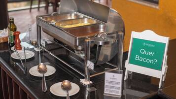 A buffet setup with a sign asking 'Quer Bacon?' indicating a bacon option.