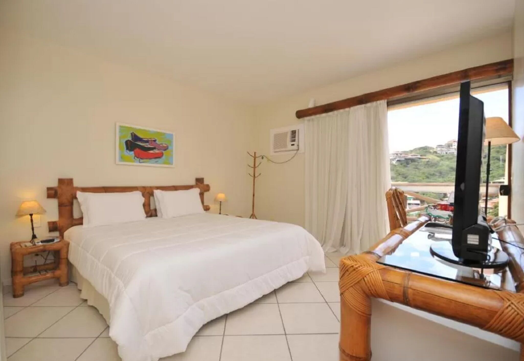 A hotel room with a bed, bedside lamps, a TV, a dining table, and a view of the outside.