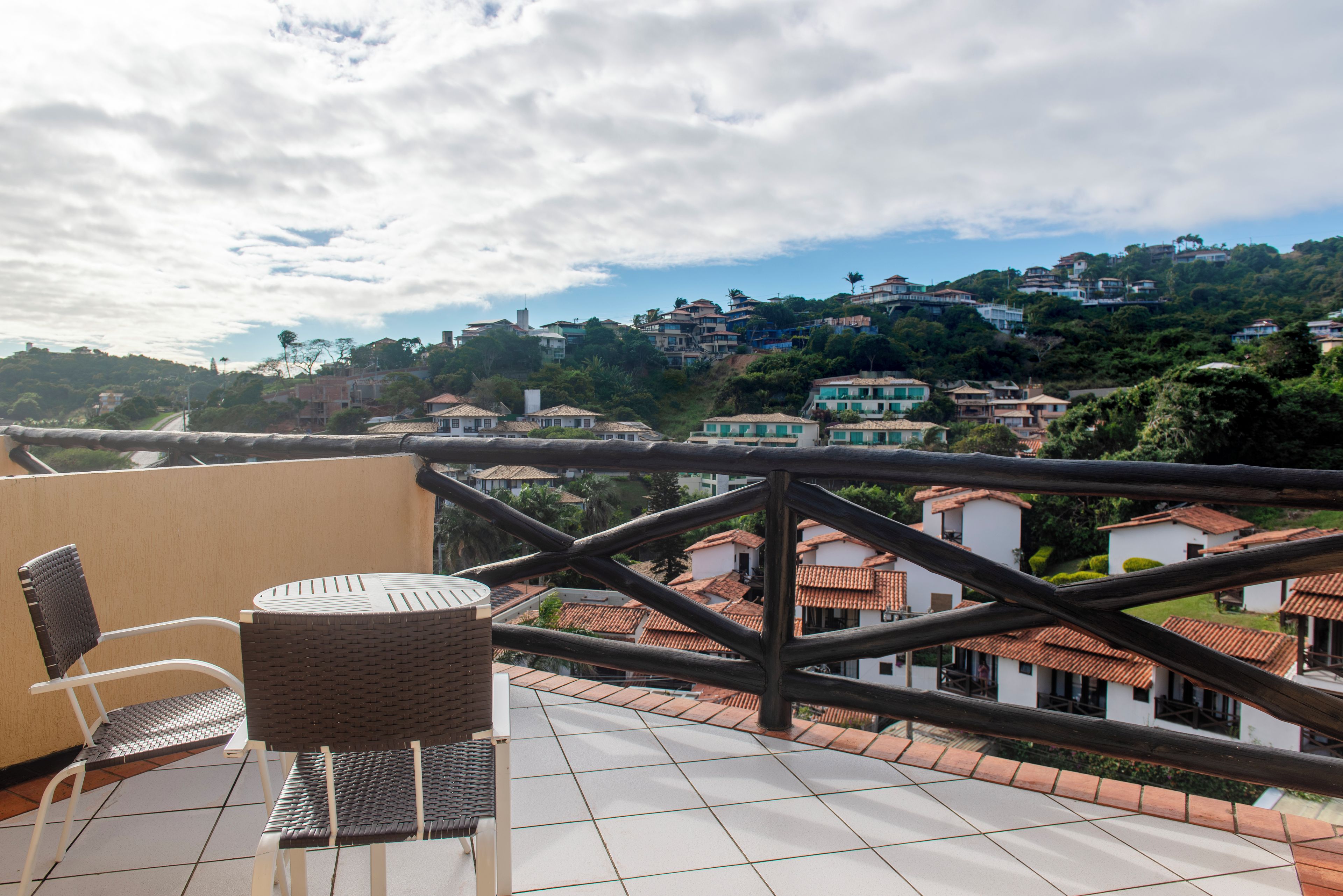 A terrace with a view of a hillside town, a wicker chair, and a tiled floor.