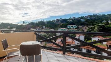 A terrace with a view of a hillside town, a wicker chair, and a tiled floor.
