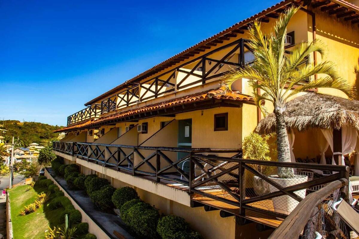 Un edificio de dos pisos con un balcón, una estructura de techo de paja y una palmera.