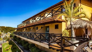 Un edificio de dos pisos con un balcón, una estructura de techo de paja y una palmera.