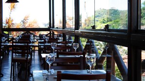 Un restaurant avec des tables et des chaises, de grandes fenêtres et une vue sur la verdure.