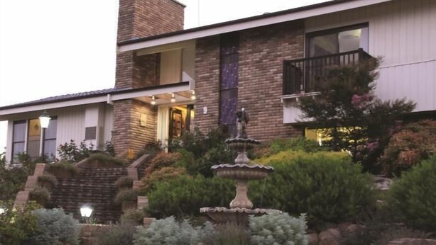 A two-story house with a stone facade, a front entrance, and a landscaped garden with a fountain. - Bathurst Heights B&B (Bathurst)